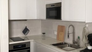 Una cucina moderna con mobili bianchi, forno integrato, microonde, lavandino e zona pranzo con tavolo.