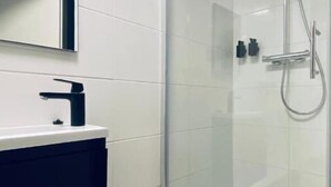 Un baño moderno con ducha envuelta en vidrio, pared de azulejos blancos y tocador oscuro.