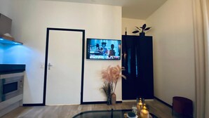 Una sala de estar moderna con un televisor de pantalla plana montado en la pared, una mesa de centro de vidrio con velas y un jarrón decorativo con plumas de pampa.