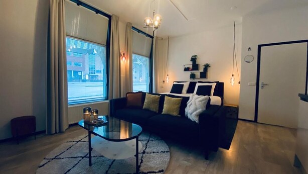 Una sala de estar moderna con un sofá negro, una mesa de centro de cristal y un amplio ventanal con cortinas.