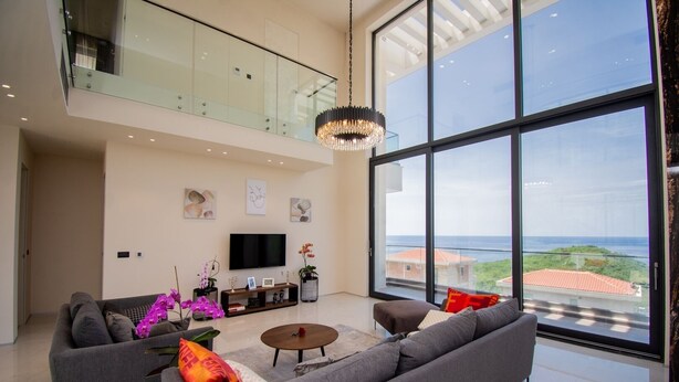 Un salon moderne avec une grande télévision, des canapés gris, une table basse et une vue sur la mer.
