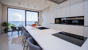 Une cuisine moderne dotée d’un grand îlot central, d’appareils électroménagers intégrés et offrant une vue sur la mer.