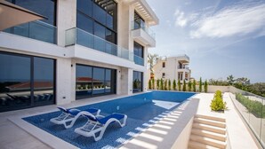 Un immeuble résidentiel moderne doté d’une piscine, d’un espace extérieur aménagé et offrant une vue dégagée sur la mer.