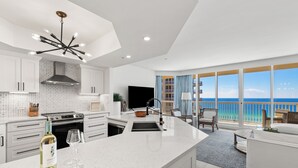 A modern kitchen with a large island, a dining area with a view of the ocean, and a balcony with a railing. - Ocean Aire Gulf Front Condo, Resort, Pool (Destin)
