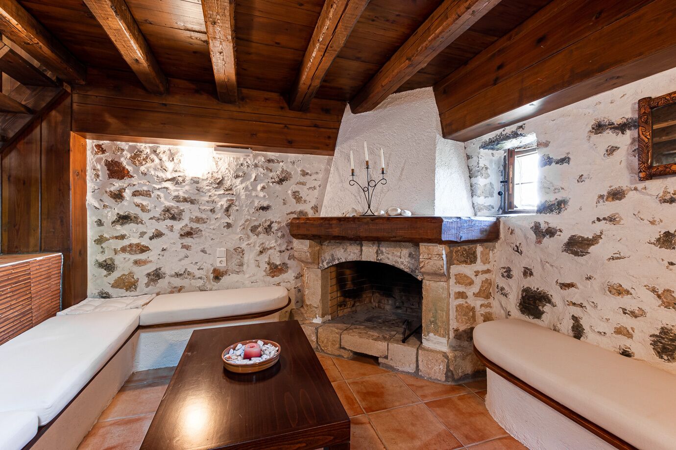 Una habitación rústica con chimenea de piedra, vigas de madera y un banco.