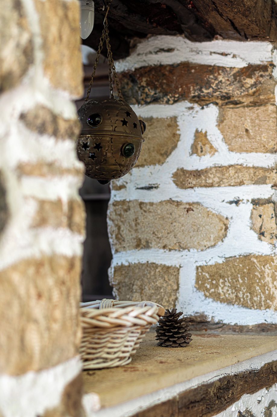 A rustic stone wall with a hanging ornament and a pine cone on a shelf.