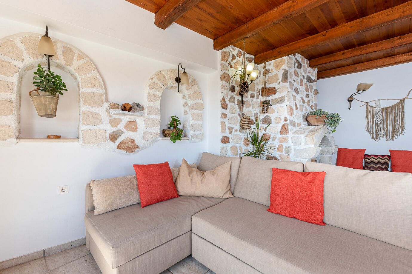 A cozy living room with a beige sectional sofa, stone wall accents, and hanging plants.