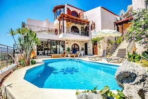 A poolside area with a clear blue pool, lounge chairs, and a staircase leading to a balcony.