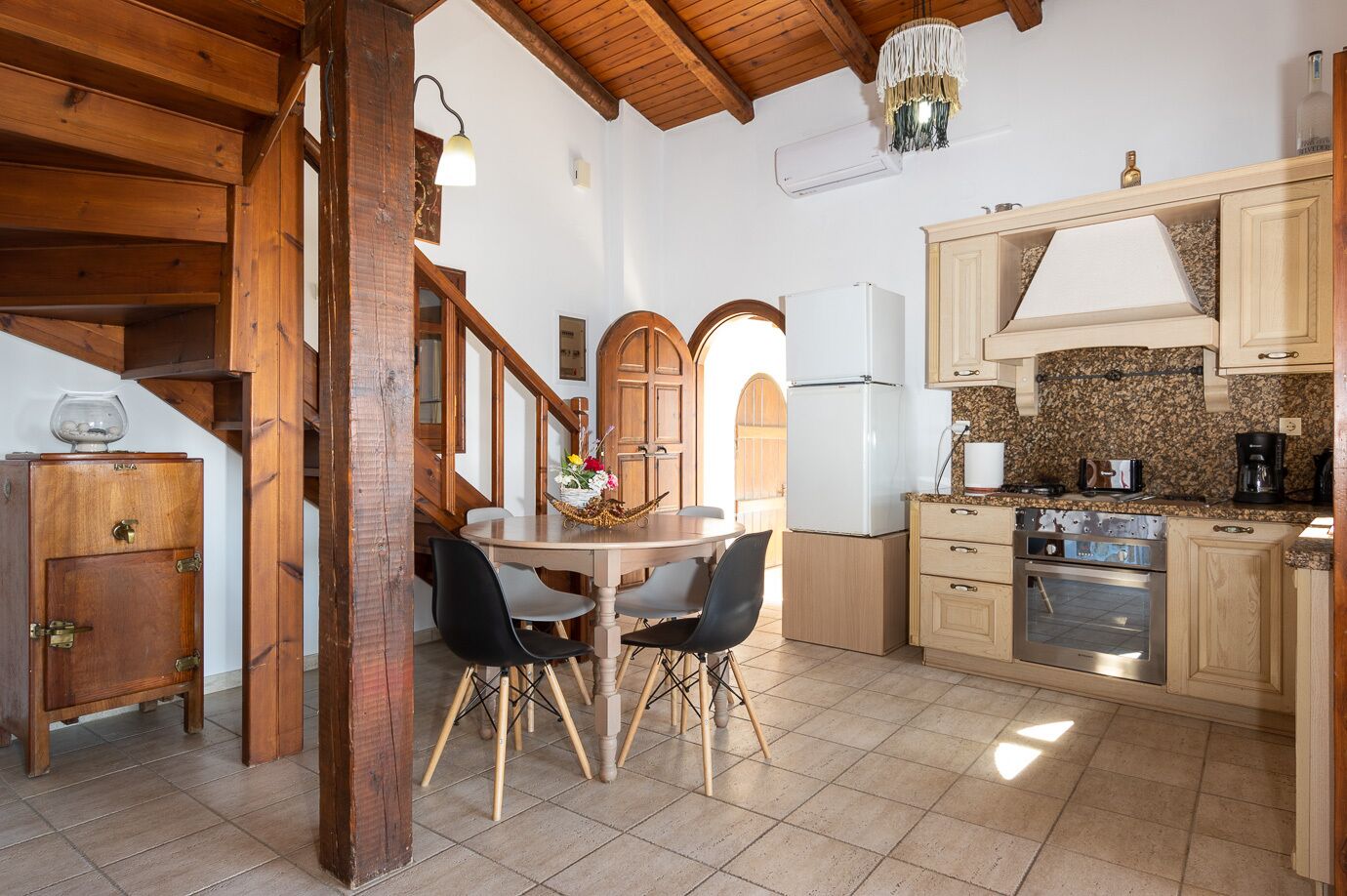 Eine rustikale Küche mit Holzschränken, einem Esstisch mit Stühlen, einem eingebauten Backofen und einer Treppe mit Holzwangen.