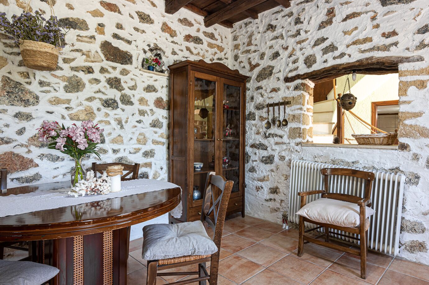A rustic stone-walled room with a wooden dining table, chairs, and a cabinet.