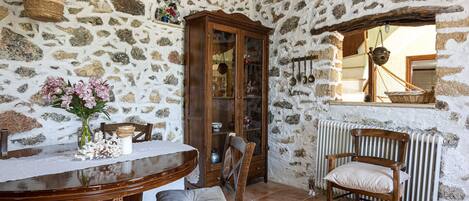 A rustic stone-walled room with a wooden dining table, chairs, and a cabinet.