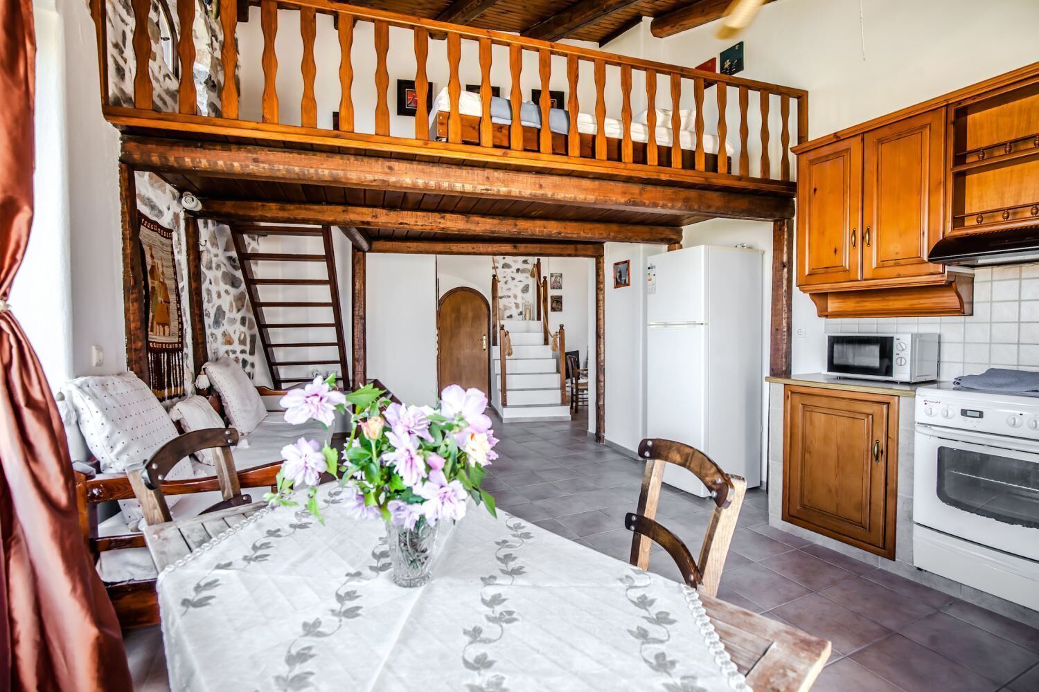 A cozy kitchen with wooden cabinets, a dining table with chairs, and a balcony with a wooden railing.