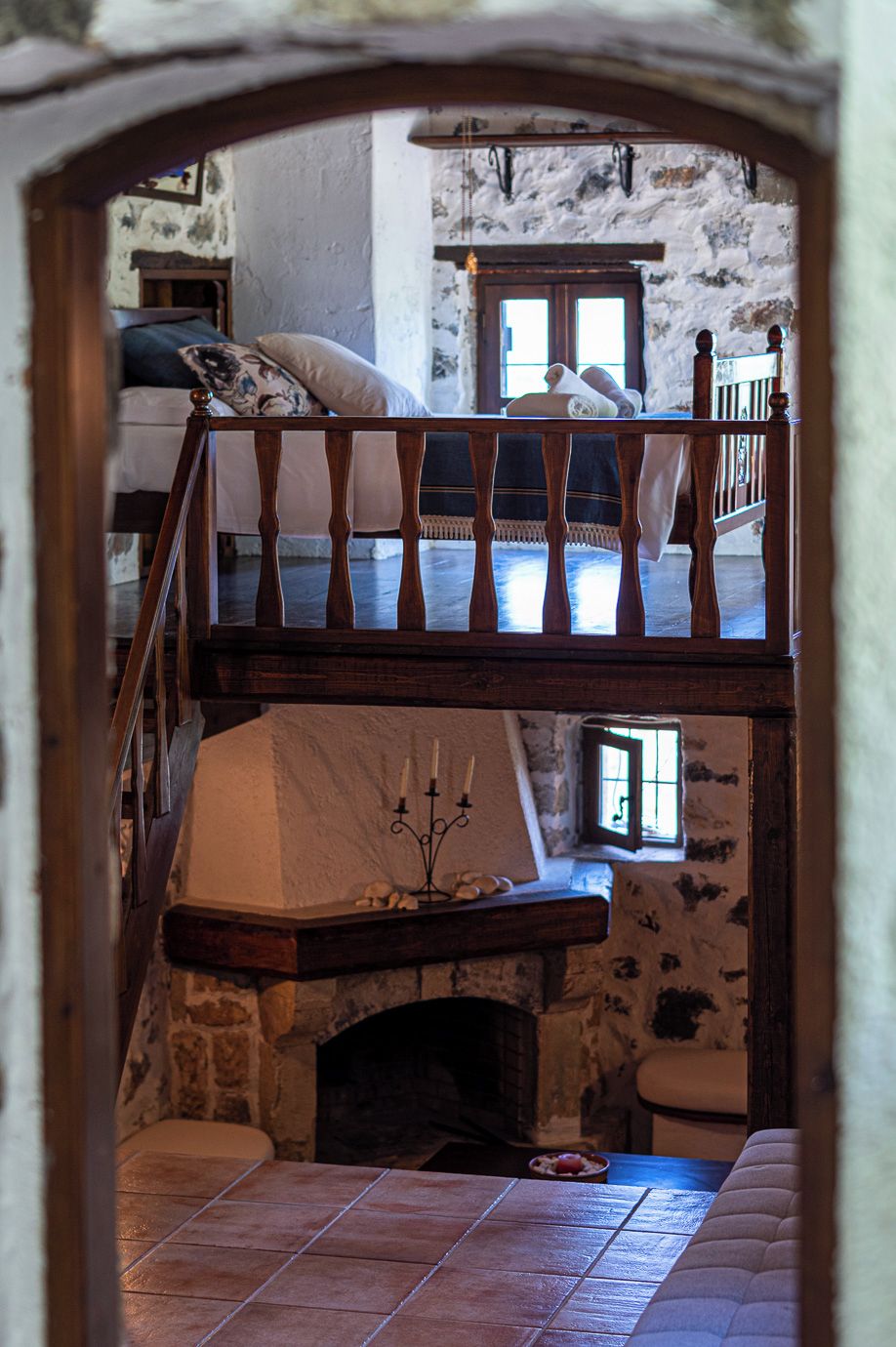 A rustic room with a wooden staircase, a stone fireplace, and a bed with a pillow.