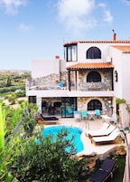 A two-story house with a swimming pool, outdoor seating, and a stone facade.