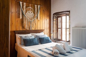 A wooden-paneled bedroom with a bed, patterned pillows, a macrame wall hanging, and a stone wall window.