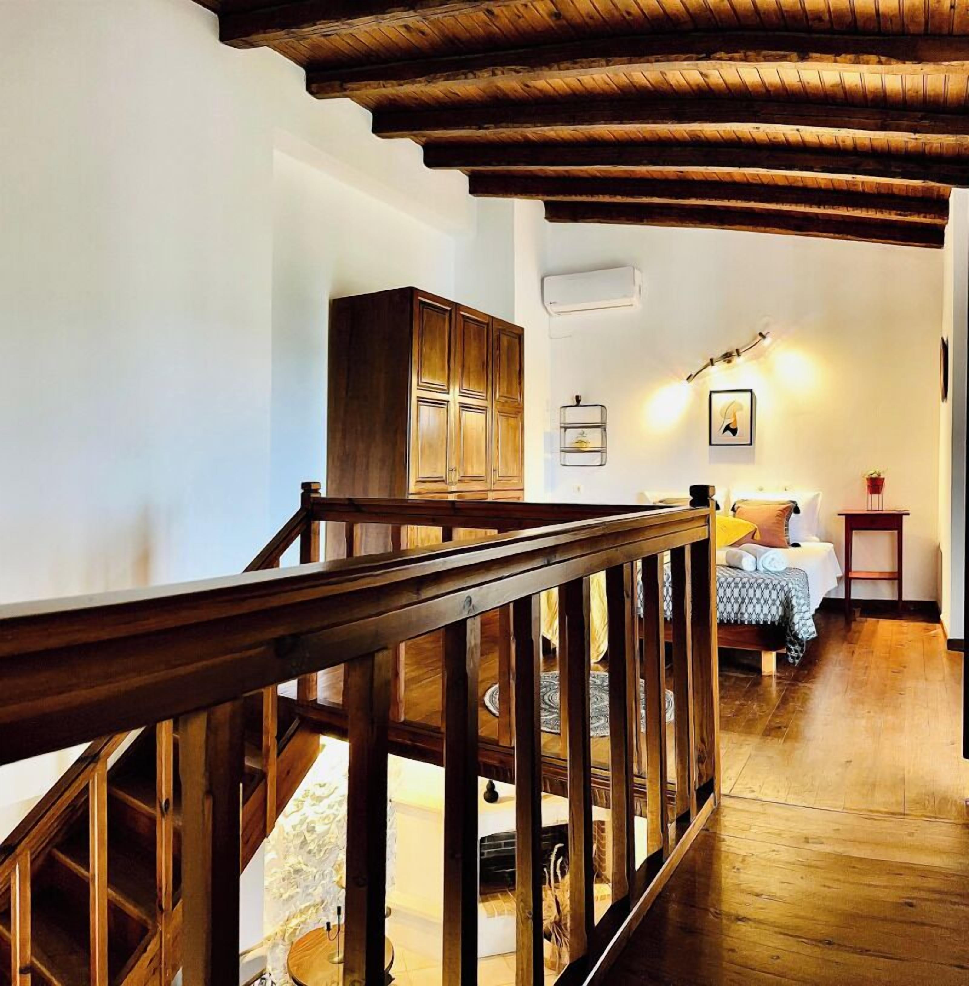 Una scala in legno conduce a una camera da letto con un letto, un comodino e una mensola a parete.