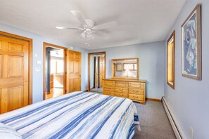 A bedroom with a bed, wooden wardrobe, dresser, ceiling fan, and framed artwork on the wall. - Stunning Beach House with an in-ground pool! (Wells)