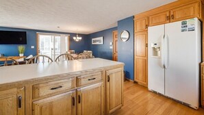 Een keuken met houten kasten, een witte koelkast, een eettafel met stoelen en een kroonluchter.