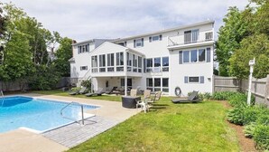 Een tweelaags huis met een zwembad, terras en een omheinde tuin.