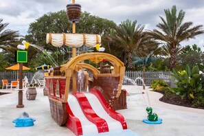 A pirate-themed water play area with a ship structure, a red and white slide, and a green frog-shaped water feature.