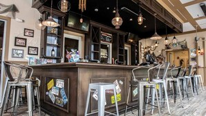 Uma área de bar com balcão, banquetas e luminárias pendentes.