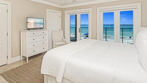 A bedroom with a large bed, a TV on a dresser, a chair, and a view of the ocean through the windows. - Gulf Front With Private Pool- Serenity Blue by Royal Destinations (Santa Rosa Beach)