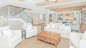A spacious living room with a staircase, white furniture, and a kitchen in the background. - Gulf Front With Private Pool- Serenity Blue by Royal Destinations (Santa Rosa Beach)