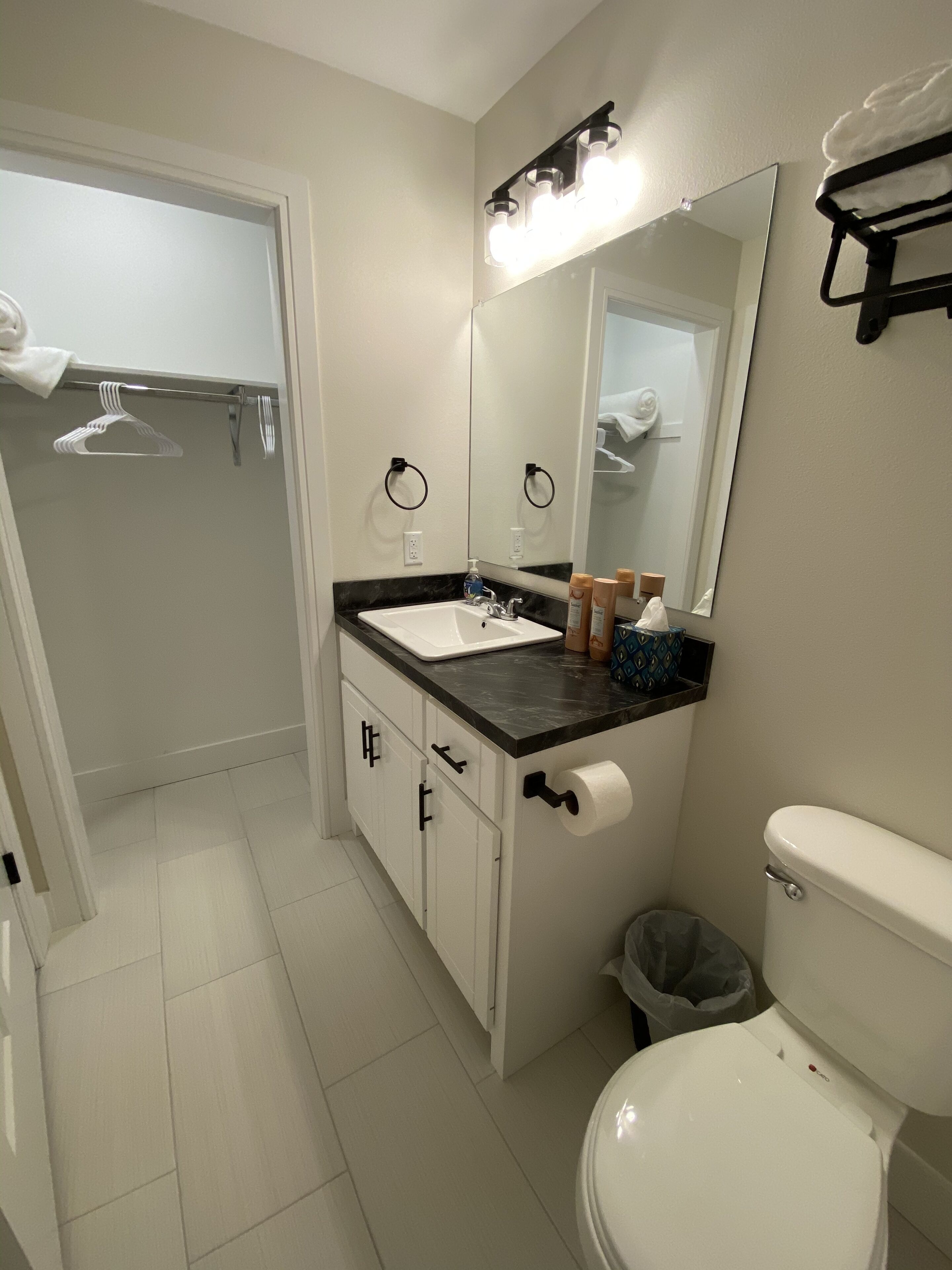 A bathroom with a white toilet, a sink with a black countertop, a mirror above the sink, and a towel rack with a white towel.