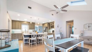 A modern kitchen with wooden cabinets, a central island with seating, and pendant lighting. - Poppy’s Hampton House | 3BR + Bonus | Near Beaches & LIRR (Hampton Bays)