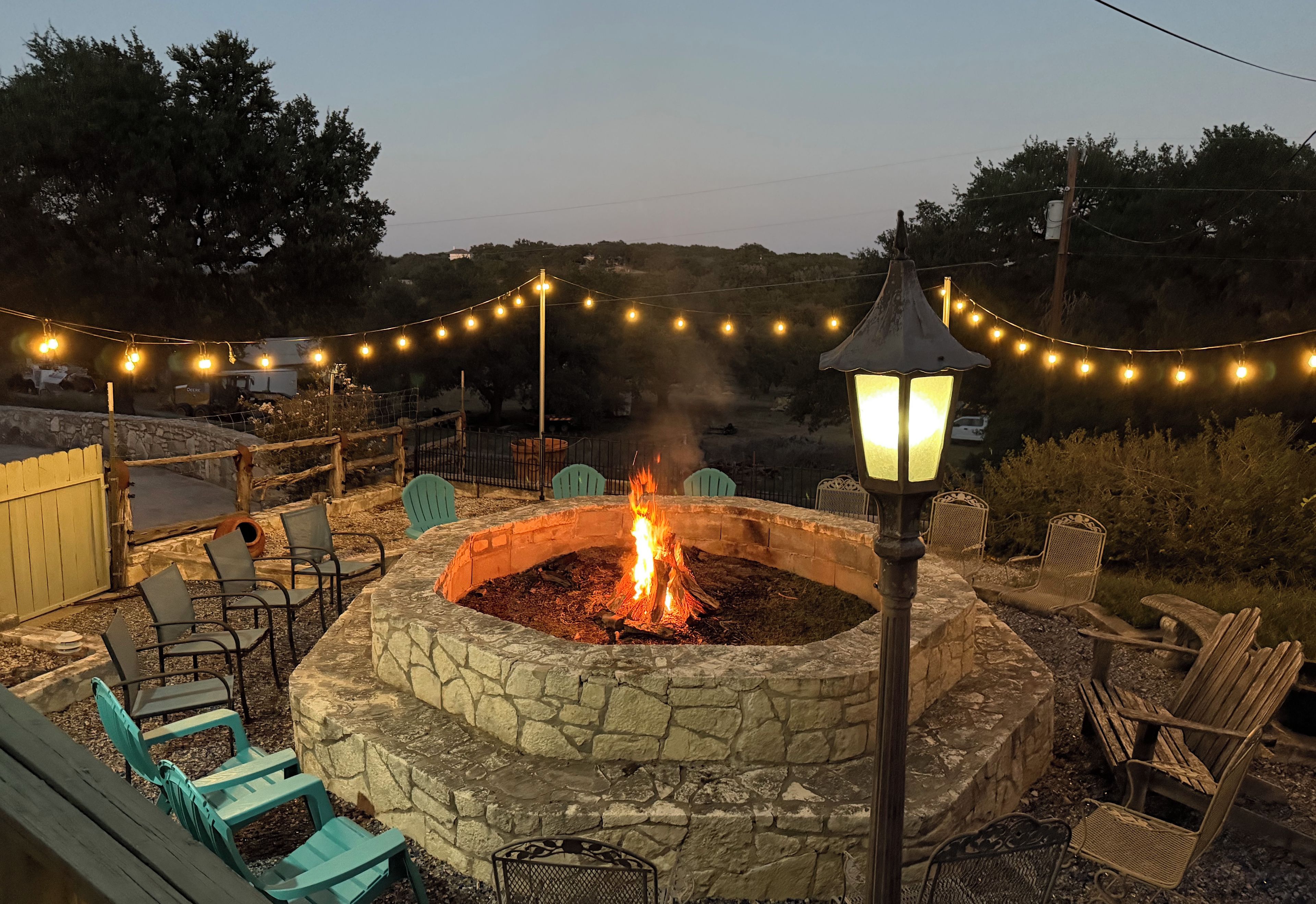 A stone fire pit surrounded by outdoor seating, string lights, and a lantern.