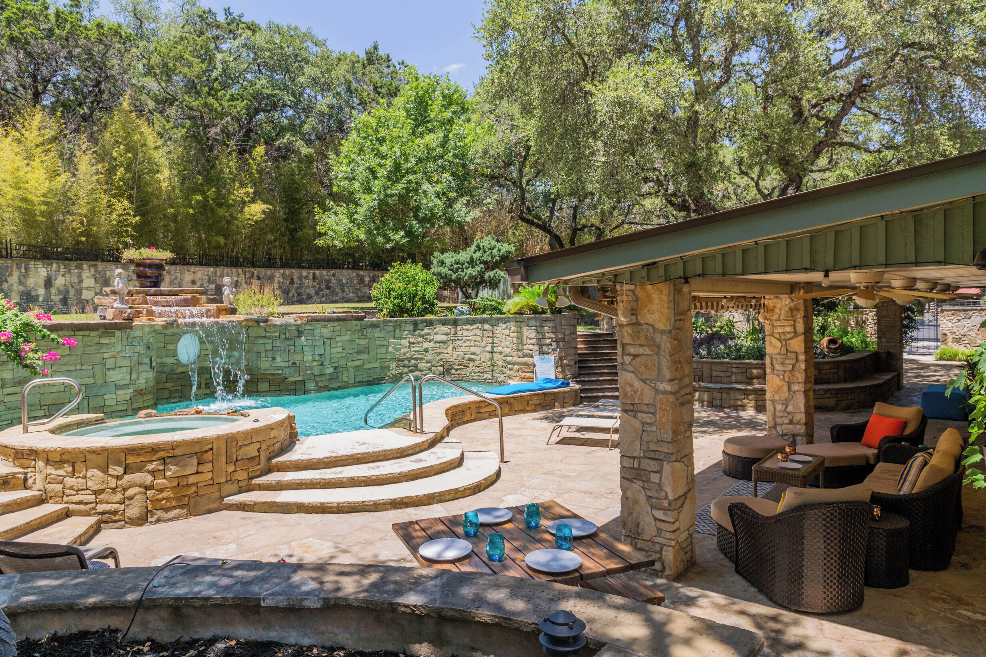 A backyard with a swimming pool, stone steps, outdoor furniture, and a pergola.