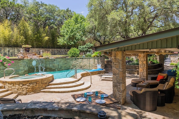 A backyard with a swimming pool, stone steps, outdoor furniture, and a pergola.