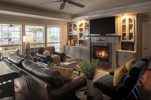 A living room with a fireplace, leather sofas, a television, and a view of the outdoors. - Your Own High-End Resort. 1-Story, HeatedPool+HotTub, BigBeds, GameRoom, FirePit (Canyon Lake)