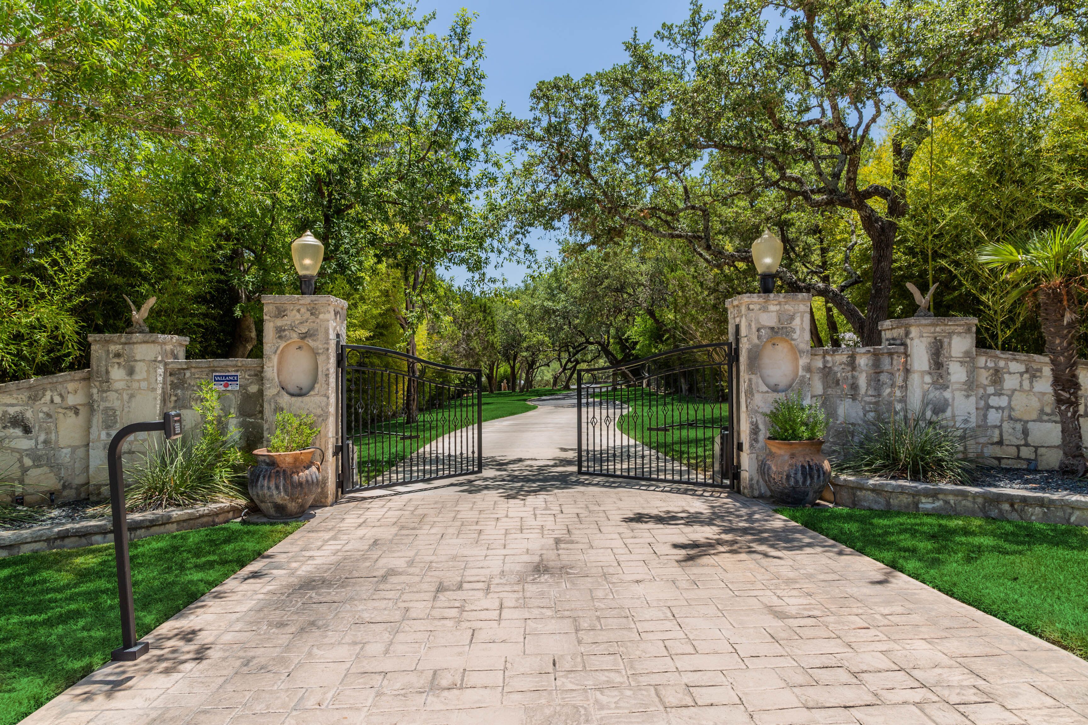 A paved pathway leading to a gated entrance with stone walls and potted plants.