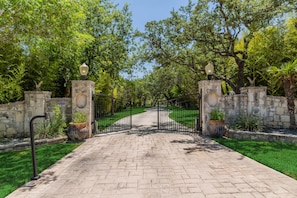 A paved pathway leading to a gated entrance with stone walls and potted plants.