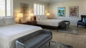 A hotel room with two beds, a grey sofa, a small armchair, and two wall-mounted lamps.