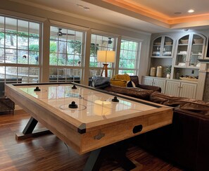 A pool table in a room with large windows, a sofa, and cabinets.