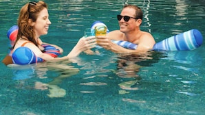 Dos personas en una piscina con flotadores, sosteniendo una bebida.