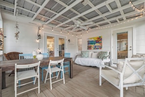 Una habitación amplia con una mesa de comedor de madera, sillas azules, un sofá blanco y una cama con ropa de cama blanca.