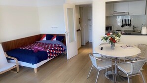 A compact room with a bed, a dining table with chairs, and a kitchenette.