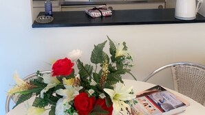 A kitchen with white cabinets, a microwave, and a kettle. There is a vase with flowers on the counter.