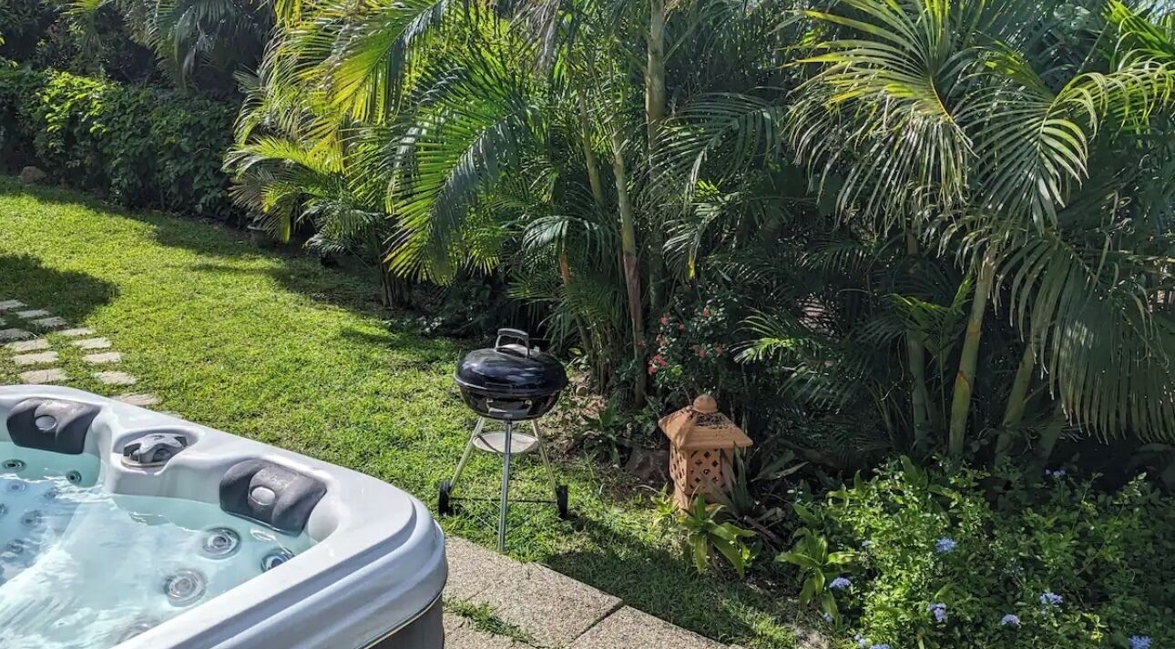 A hot tub in a lush garden with a grill and a lantern.