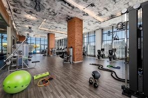 Une salle de sport équipée de divers appareils d’exercice, dotée de grandes fenêtres et d’un pilier en briques.