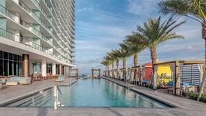 A pool area with a modern building, palm trees, and outdoor seating.