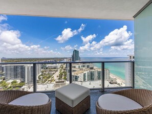 A balcony with wicker furniture, a view of the beach, and high-rise buildings.