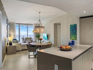 A modern kitchen with a central island, dining area with chairs, and a view to the outside.