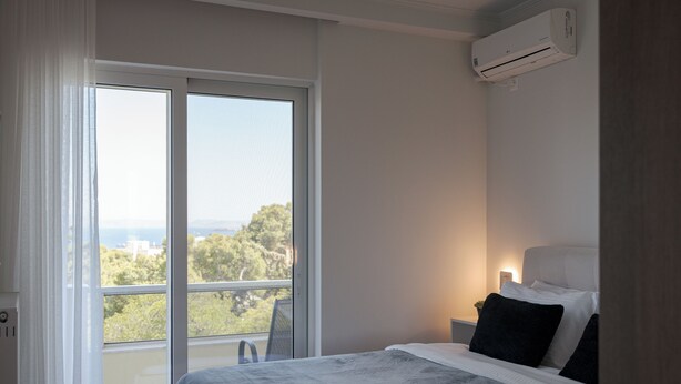 A bedroom with a large window, a bed with white and black bedding, and an air conditioning unit on the wall. - Athenian Riviera Sea View Penthouse (Vari-Voula-Vouliagmeni)