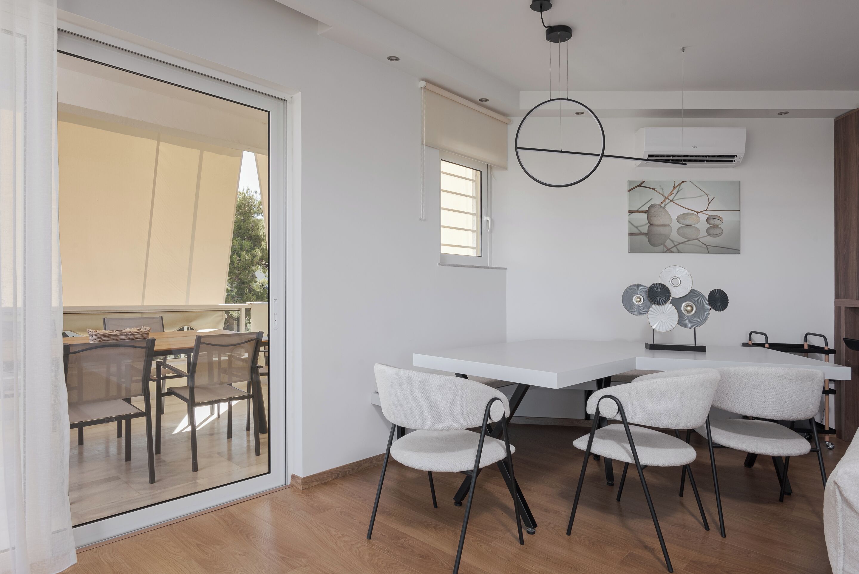 Een moderne eethoek met een witte tafel en stoelen, een groot raam met zonwering, en een plafondventilator.