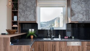 A modern kitchen with wooden cabinets, a black countertop, a built-in sink, and a window overlooking a cityscape. - Athenian Riviera Sea View Penthouse (Vari-Voula-Vouliagmeni)