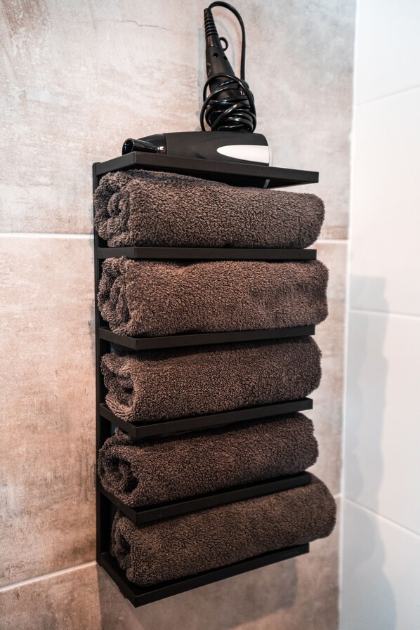 A towel rack with five folded towels against a tiled wall. - The Hogg House (Groningen)
